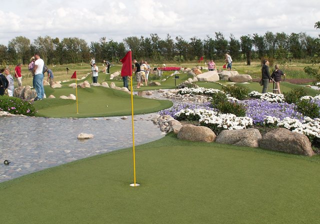 En äventyrsgolfgreen bredvid vatten och blommor